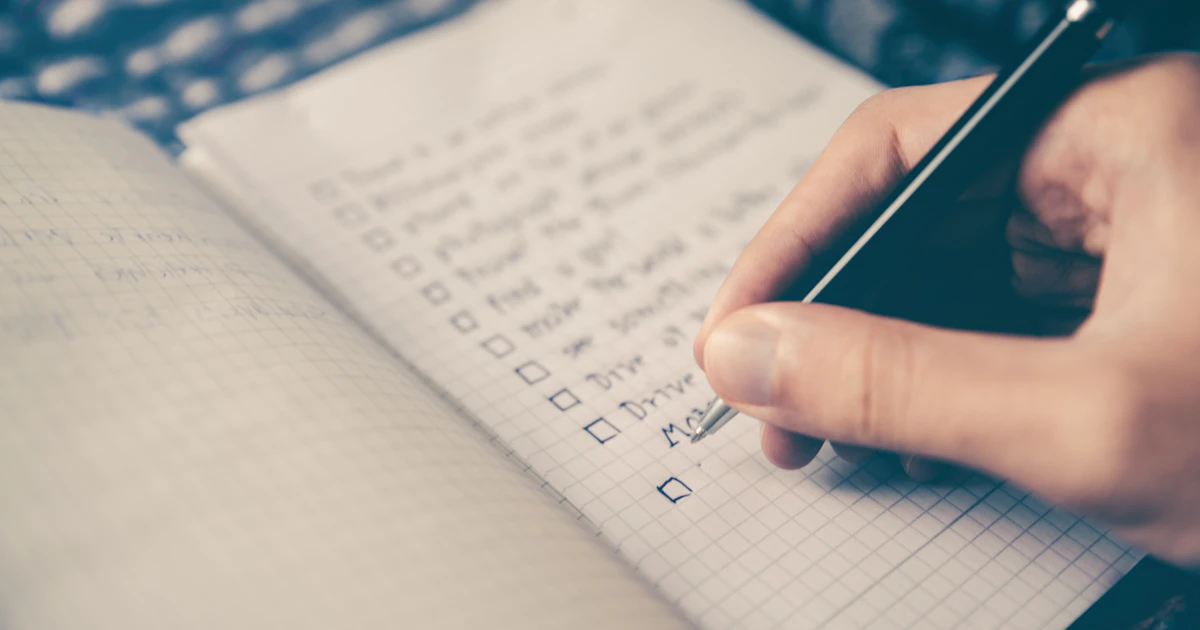 A checklist and pen on a desk next to a laptop